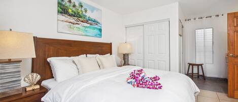 Un lit bien fait, avec du linge de lit blanc, une tête de lit en bois et, au-dessus, un tableau représentant une plage tropicale.
