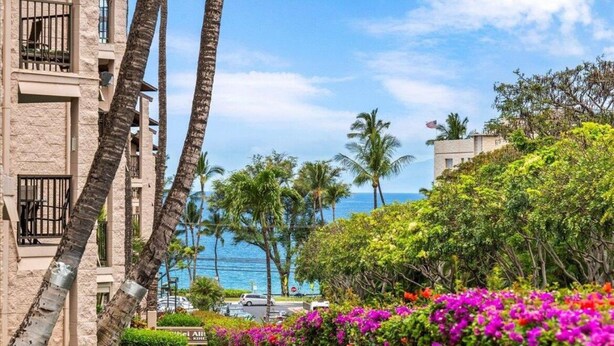 Ein Hotel mit Blick auf den Ozean, Palmen und bunten Blumen.