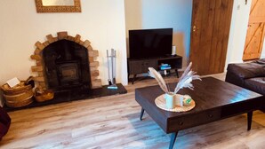 A living room with a fireplace, a television, a sofa, and a coffee table. -  Coachman’s Cottage at Brylach Steading, Speyside (Aberlour)