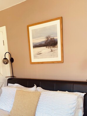 A bedroom with a bed, a framed painting, and a lamp.