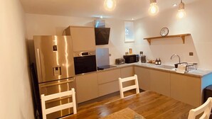 A modern kitchen with stainless steel appliances, wooden dining table, and pendant lighting. -  Coachman’s Cottage at Brylach Steading, Speyside (Aberlour)