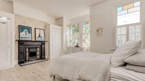 Ein Schlafzimmer mit Kamin, Bett, Kommode und einem Fenster mit Jalousien.
