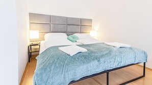 A neatly made bed with a blue quilt, two bedside lamps, and a grey headboard. - Family 2BR Stay Near Stadthalle (Vienna)