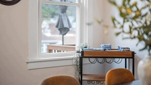 Une pièce chaleureuse avec une fenêtre donnant sur la rue, une petite table avec de la vaisselle aux motifs bleus et blancs, et une chaise.
