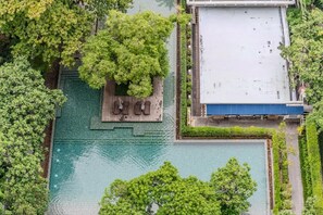 Ein Blick von oben auf einen Dachpool, umgeben von üppigem Grün, mit einer Holzterrasse und einem Gebäude mit blauem Dach im Hintergrund.