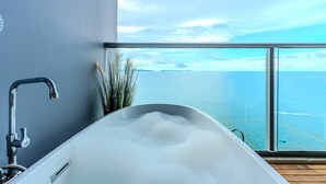 Un baño moderno con una bañera grande, un grifo a la vista y vistas al océano a través de un ventanal.