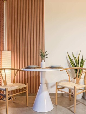 A dining area with a white table, two chairs, a vase with a plant, and a tall plant beside the table. - Zire Wongamat | Beachfront Seaview with Bathtub (Pattaya)