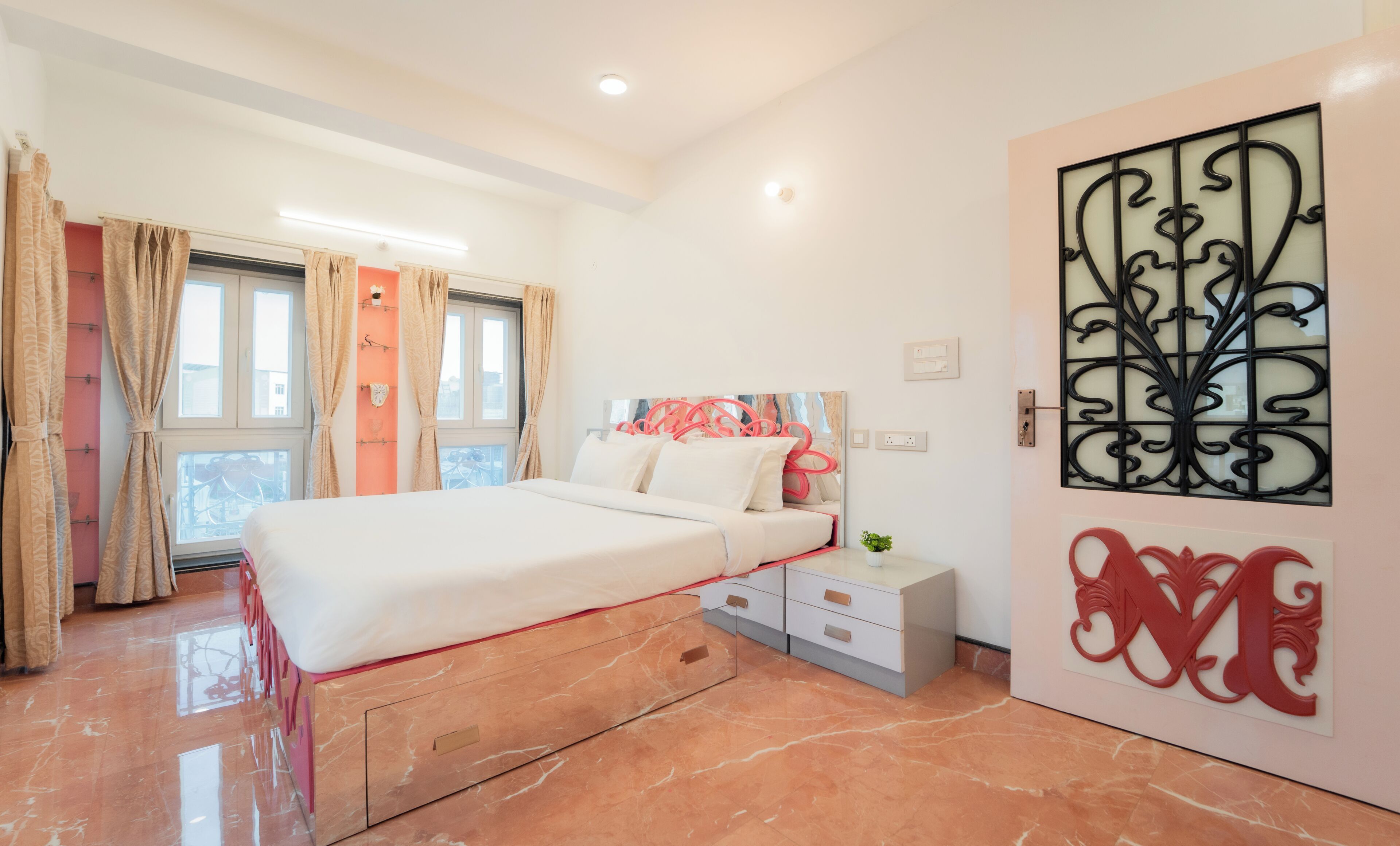 Une chambre à coucher comprenant un lit, des tables de chevet, une fenêtre avec des rideaux et un élément décoratif mural.