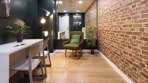 Un espacio de oficina moderno con pared de ladrillo, suelo de madera, un escritorio con sillas y un sillón verde.