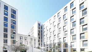 Un edificio moderno con varios pisos, grandes ventanales y un patio con zonas de estar y vegetación.