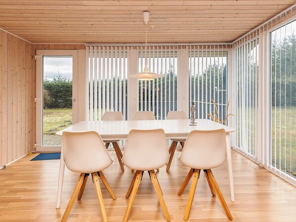 A modern dining area with a wooden ceiling, a large table with chairs, and a view through a glass door.
