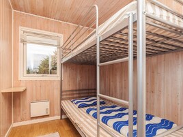A bunk bed room with wooden walls, a window with blinds, and a small shelf.