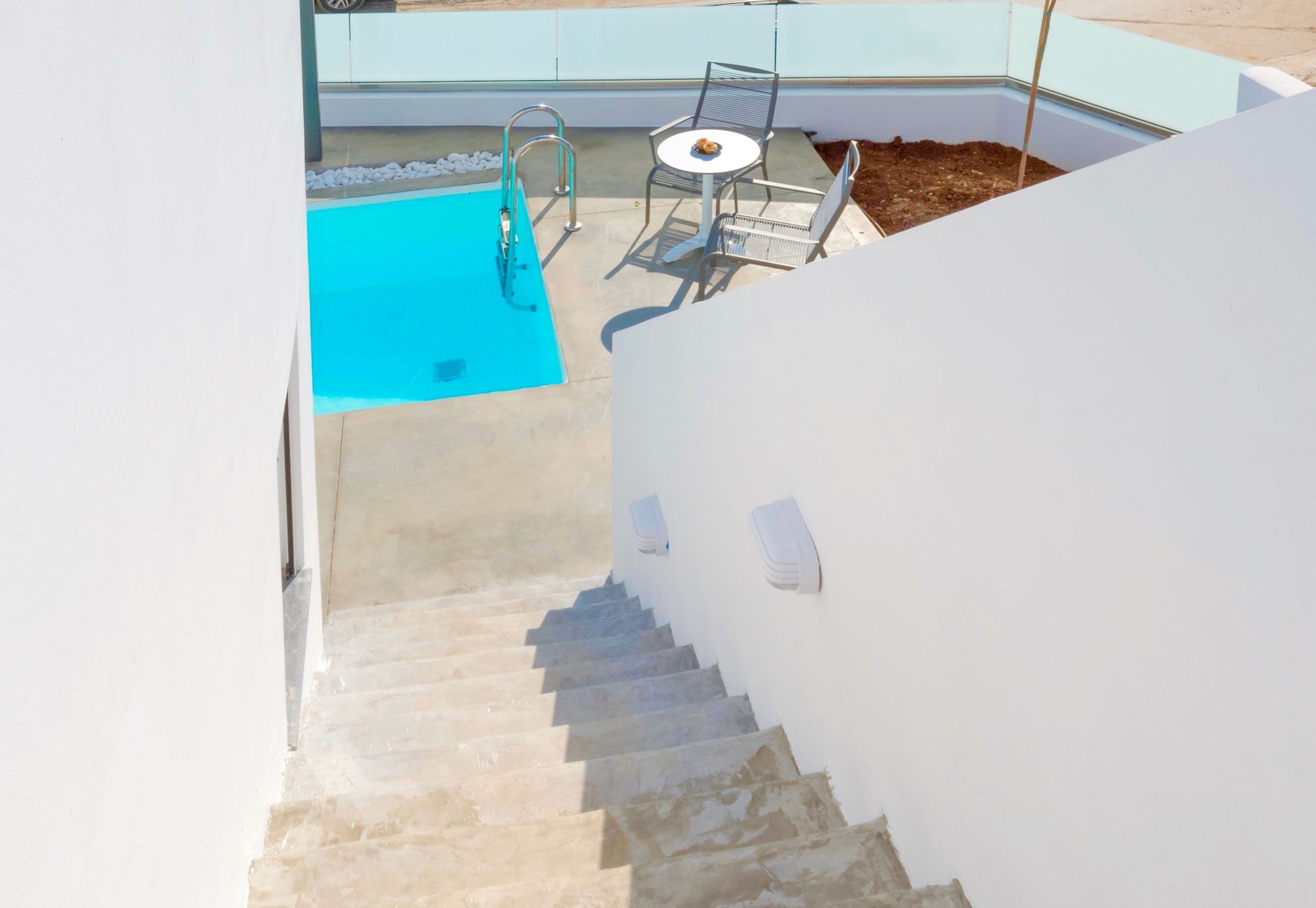 Un espace piscine avec une piscine bleue, une chaise en métal et une table.