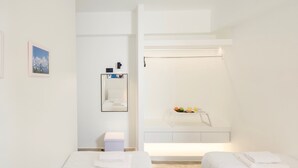A minimalist hotel room with two beds, a small bedside table, a mirror, and a shelf with toiletries. - Villa Paradiso 1 With Private Pool (Malevizi)