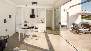 A modern kitchen with white cabinets, a black range hood, and a dining area with white chairs and a table. - Villa Paradiso 1 With Private Pool (Malevizi)