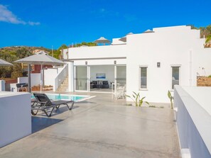 Una casa moderna de color blanco con piscina, mobiliario exterior y una escalera que lleva a un espacio cubierto.