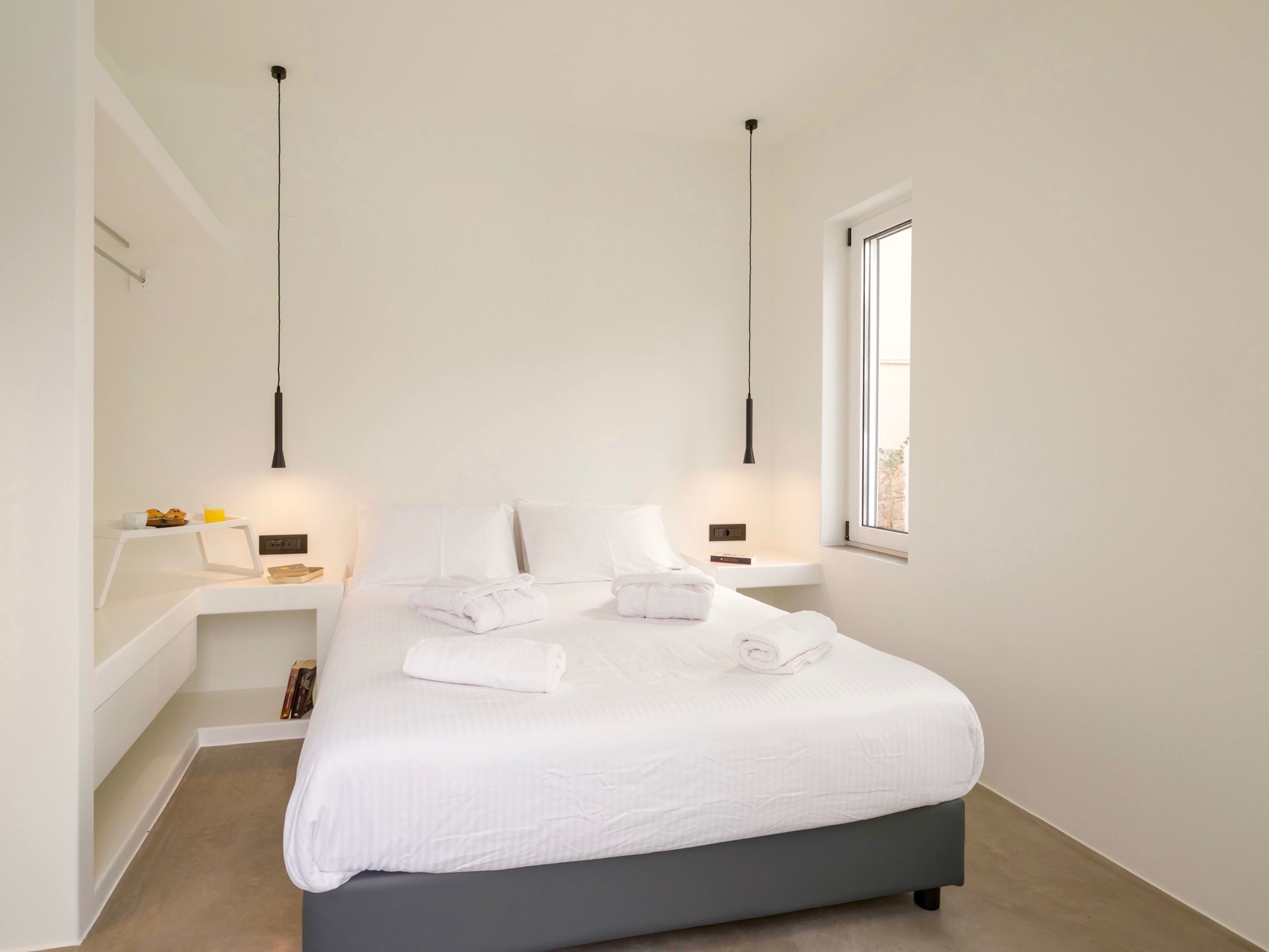Un dormitorio moderno con una cama grande, mesitas de noche, una ventana y lámparas colgantes.