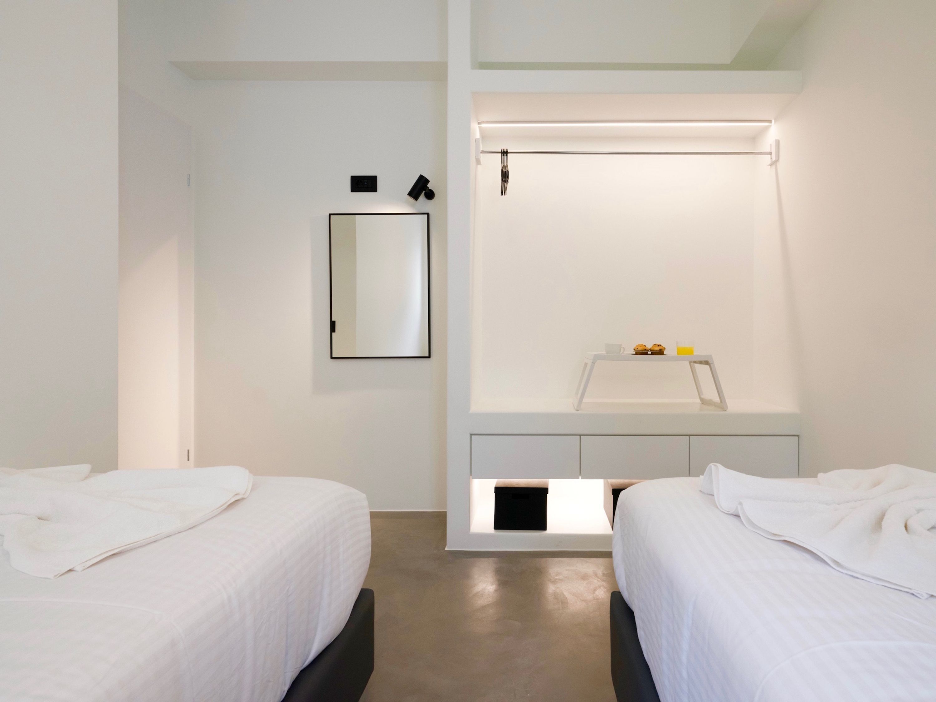 A modern hotel room with two beds, a built-in desk with a mirror, and a small breakfast area.