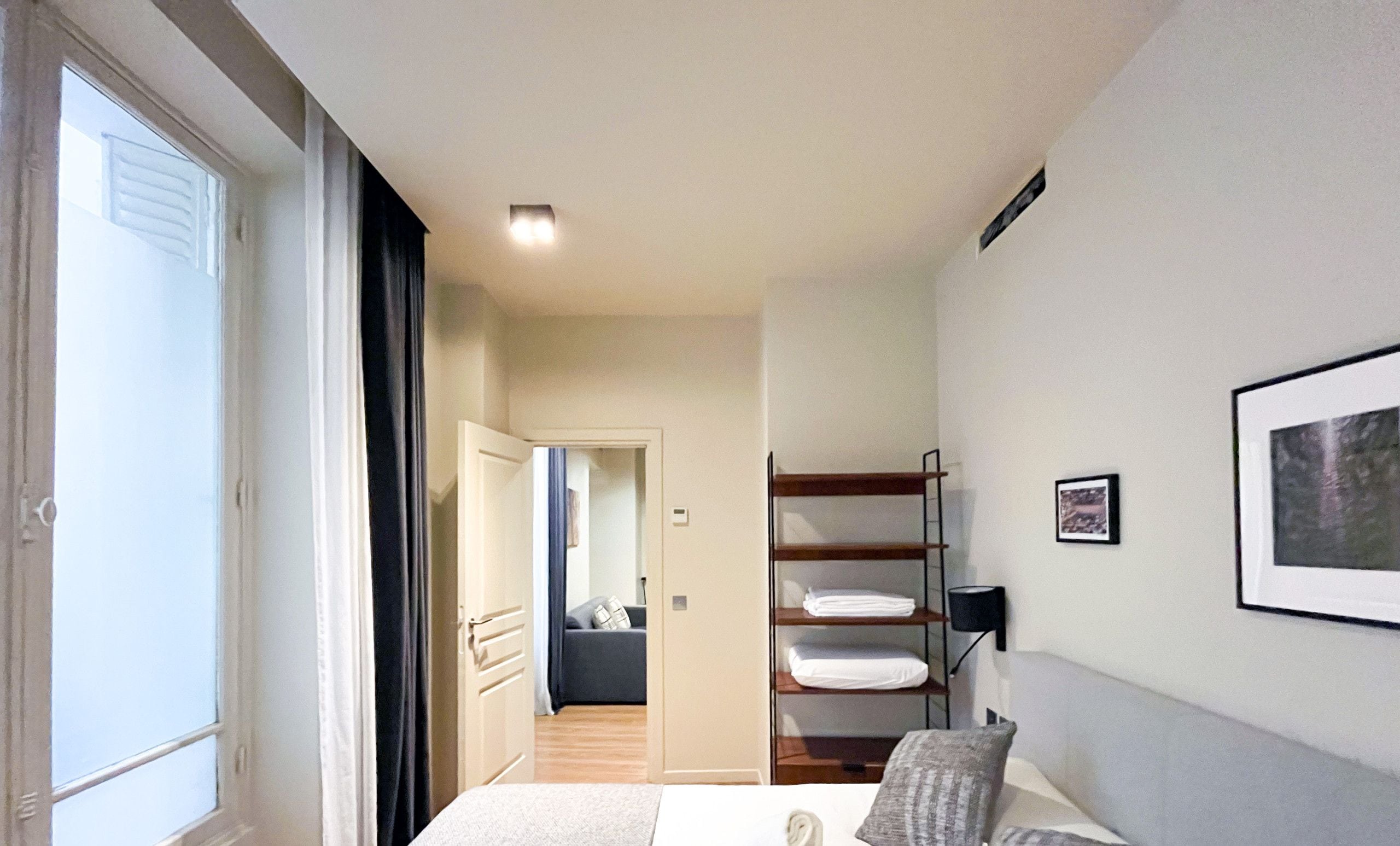 A hotel room with a bed, a bedside table, a wardrobe, a window, and a door.