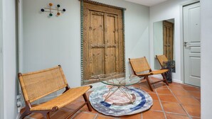A hallway with two wicker chairs, a glass table, and a wooden door with intricate carvings.