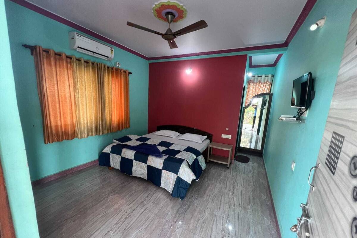 A bedroom with a bed, an air conditioner, a ceiling fan, and a television.