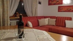 Ein Wohnzimmer mit einem roten Sofa, einem Tisch mit einer Weinflasche und einem Glas sowie blumigen Vorhängen.