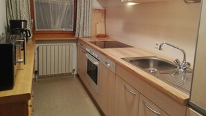 Eine kleine Küche mit Holzschränken, einem Backofen, einer Spüle und einem Fenster mit Vorhängen.