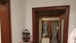 Ein Flur mit einem Holztürrahmen, einer kleinen Ablage mit Vogelkäfig und einem Blick in einen Raum mit Bett und Vorhängen.