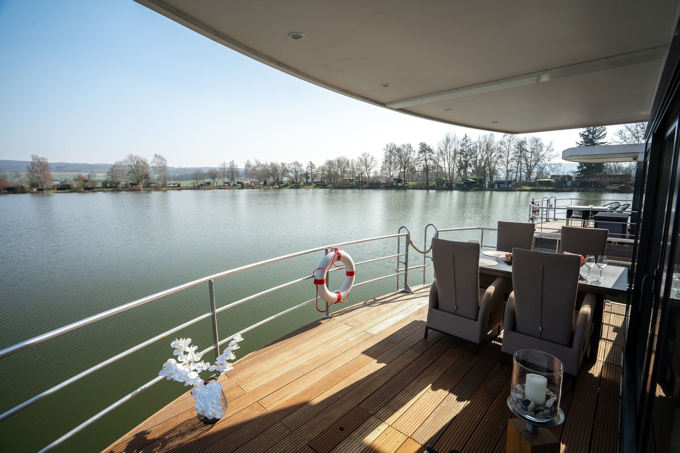 Una terraza con mobiliario exterior, un flotador salvavidas y vistas a un lago tranquilo.