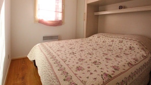 A bedroom with a floral bedspread, a window with blinds, a built-in wardrobe, and a radiator. - T2 Luchon Center - Balcony - Parking Included - Pets Welcome (Bagnères-de-Luchon)