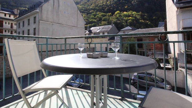 A balcony with a round table, two chairs, and two wine glasses. - T2 Luchon Center - Balcony - Parking Included - Pets Welcome (Bagnères-de-Luchon)
