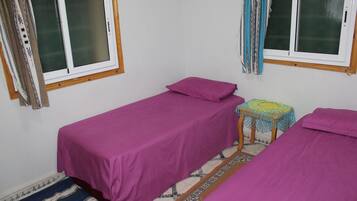A small, simple room with two beds, a small table, and a window with curtains.