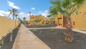 A pathway leading to a yellow building with a palm tree in the foreground. - Vacation Apartment 'Casa Piña Colada' with Balcony and Wi-Fi (Corralejo)