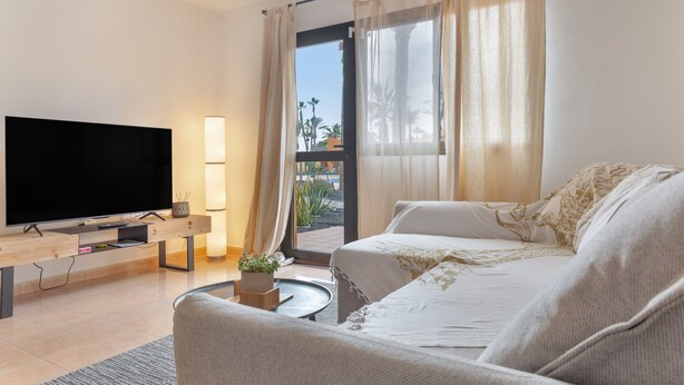 A modern living room with a flat-screen TV, a sofa, a coffee table, and a balcony with curtains. - Vacation Apartment 'Casa Piña Colada' with Balcony and Wi-Fi (Corralejo)