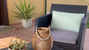 A wicker chair with a cushion, a small table with a plant and a basket, and a potted plant. - Vacation Apartment 'Casa Piña Colada' with Balcony and Wi-Fi (Corralejo)
