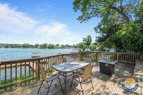 A wooden deck with a table and chairs, overlooking a lake with boats.