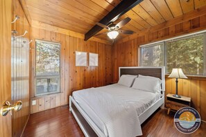 Un dormitorio con paneles de madera, una cama, un ventilador de techo y una mesita de noche con una lámpara.