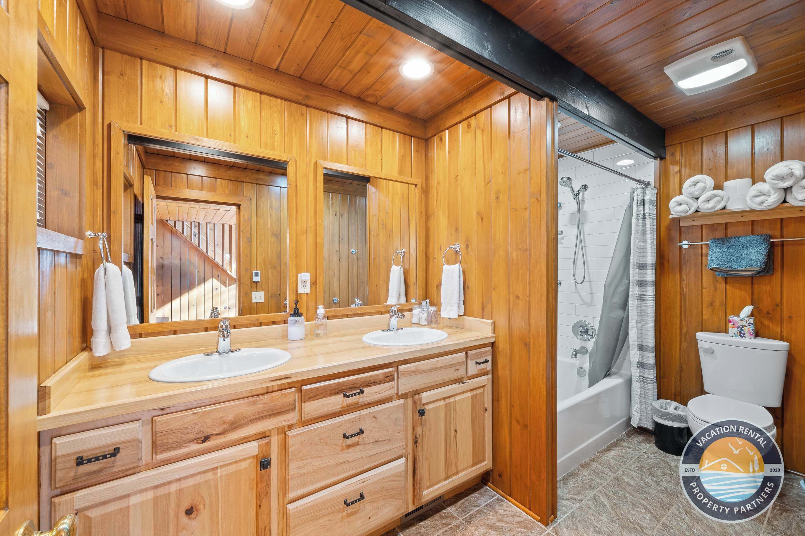 Ein Badezimmer mit Holzeinrichtung, zwei Waschbecken, einer Dusche und einem WC.