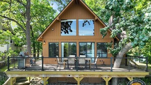 Une maison de vacances en bois dotée d’une terrasse, de grandes fenêtres et de fondations en pierre.