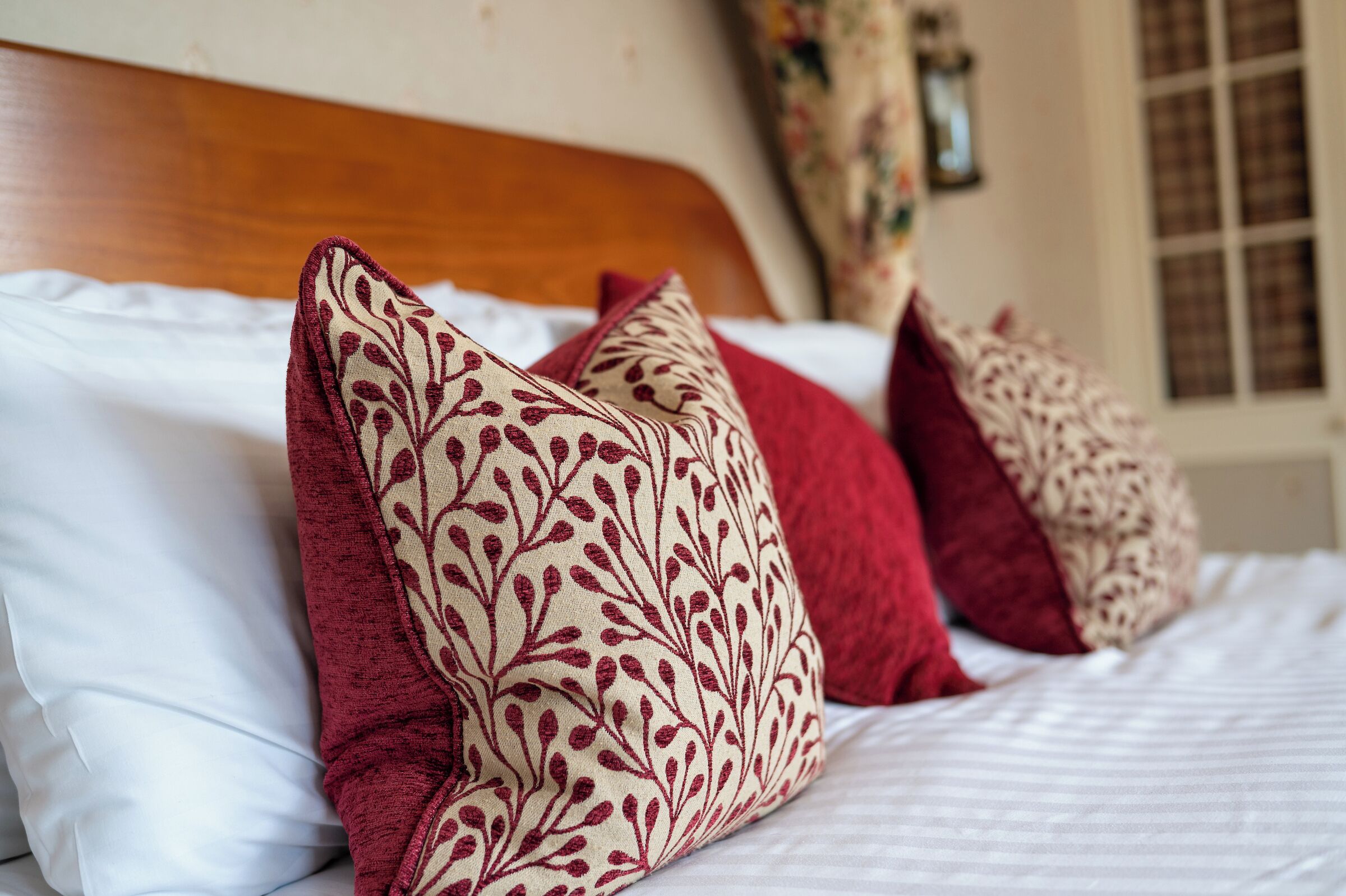 A bed with white linens and multiple decorative pillows with a leaf pattern.