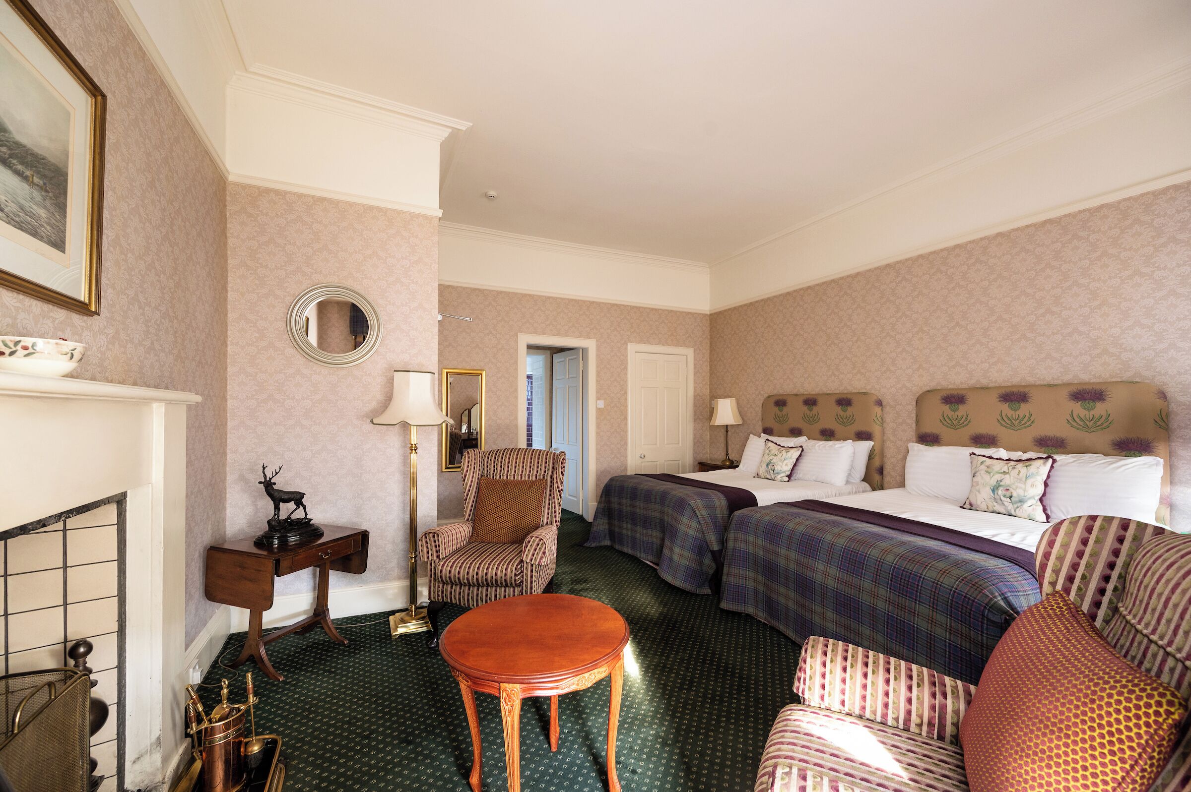 Habitación de hotel con dos camas, una zona de estar con una mesa, una silla y un espejo.