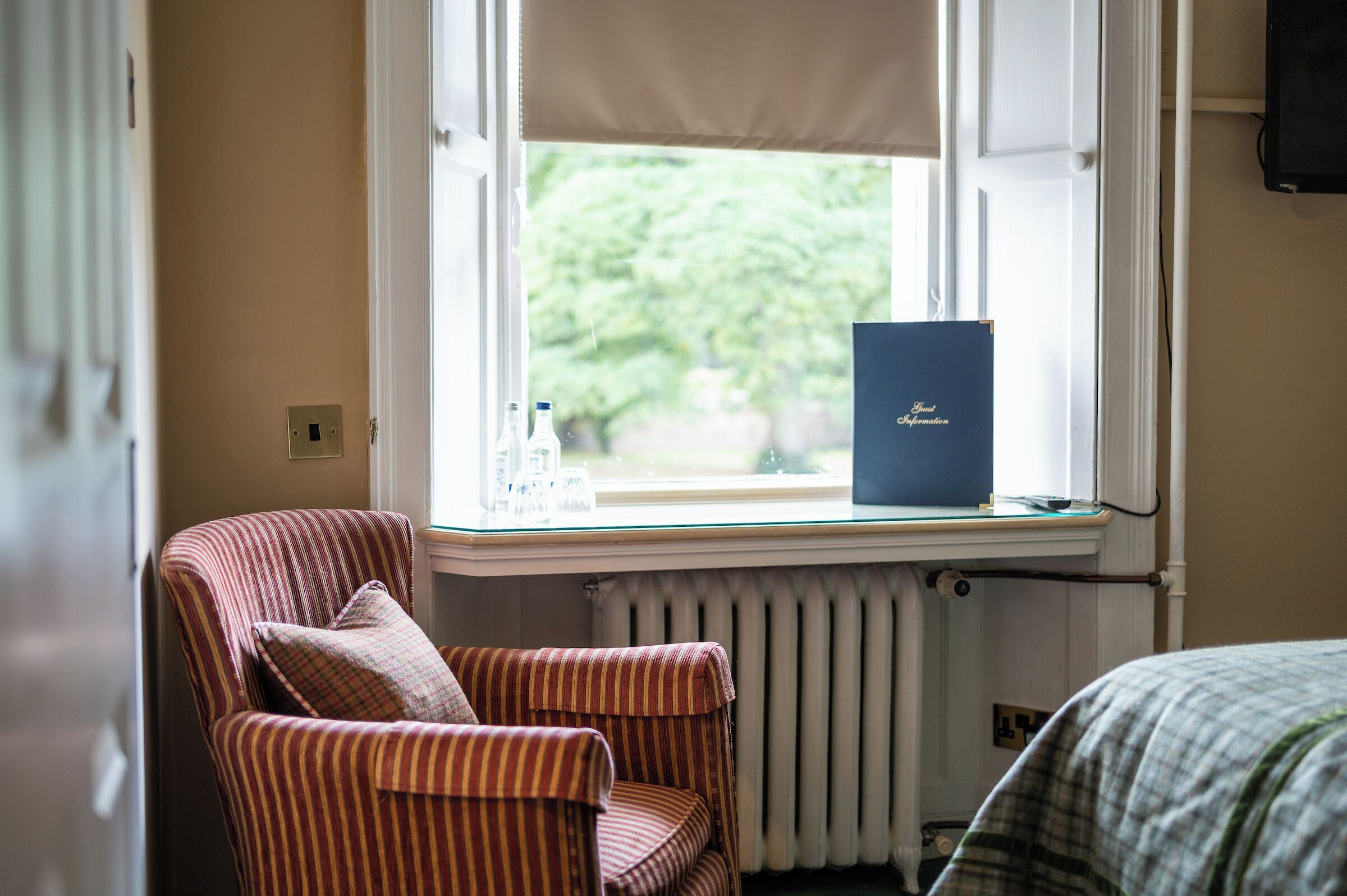 A room with a striped armchair near a window, a radiator, and a blue folder on the windowsill.