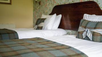 Habitación de hotel con dos camas, cada una con una manta y almohadas a cuadros, y papel tapiz con motivos florales.