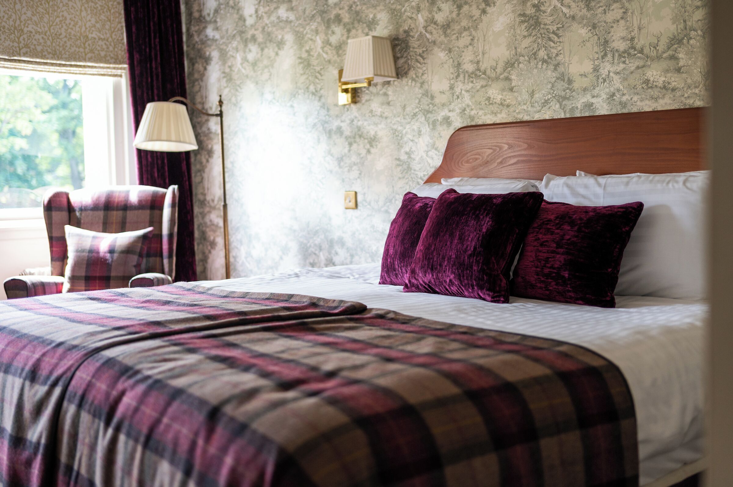 A hotel room with a plaid bedspread, a wooden headboard, and a plaid armchair.
