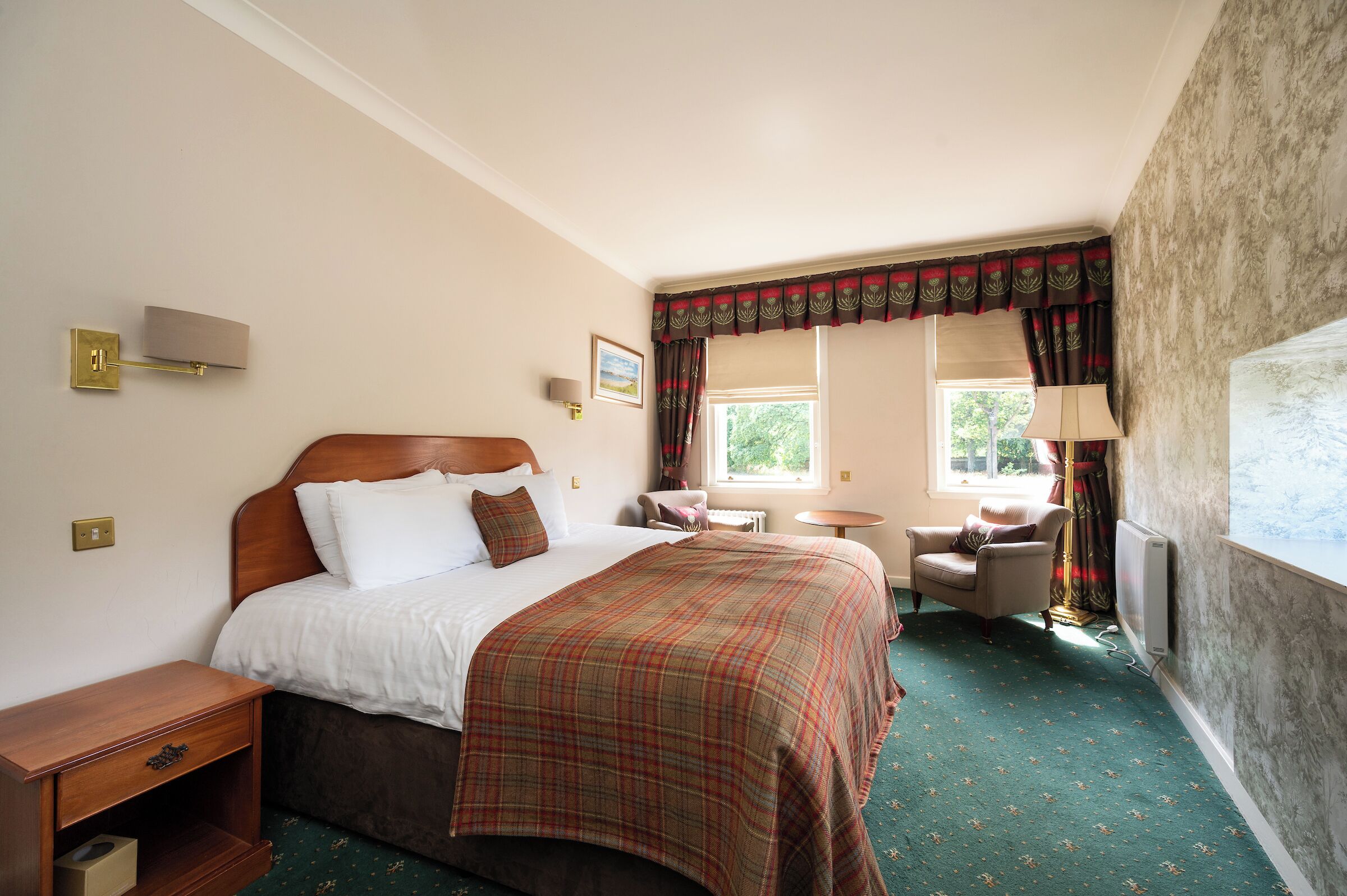 A hotel room with a large bed, a bedside table, a chair, a small table, and a window with curtains.