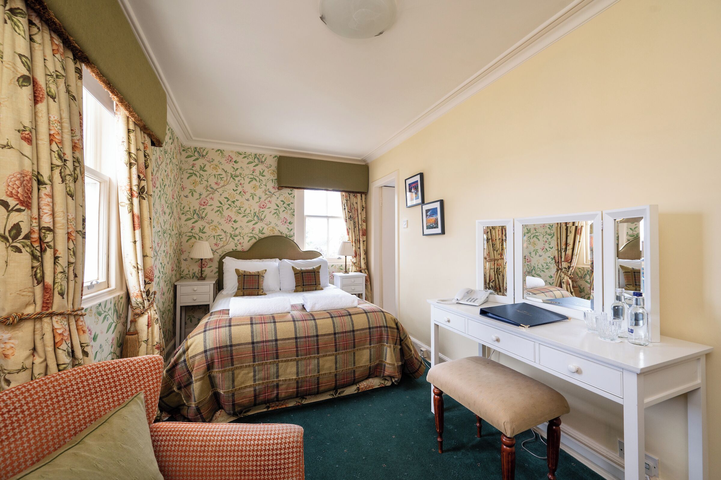 A bedroom with a bed, a bedside table, a dresser, a mirror, and a window with curtains.