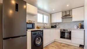 A modern kitchen with stainless steel appliances, white cabinetry, and a large window providing natural light. - Piscine-Jacuzzi-Videoprojector-Clim La Perle Rare (Mougins)