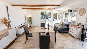 A modern kitchen with a wooden ceiling, a dining table with chairs, a sofa, and a small cabinet. - Piscine-Jacuzzi-Videoprojector-Clim La Perle Rare (Mougins)