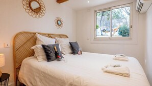 A bedroom with a large bed, a window with a view of the outside, and a wooden ceiling beam. - Piscine-Jacuzzi-Videoprojector-Clim La Perle Rare (Mougins)