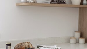 A kitchen counter with a loaf of bread, a knife, a jar of jam, and a white cloth. - Costal Comfort (Nelson Bay)